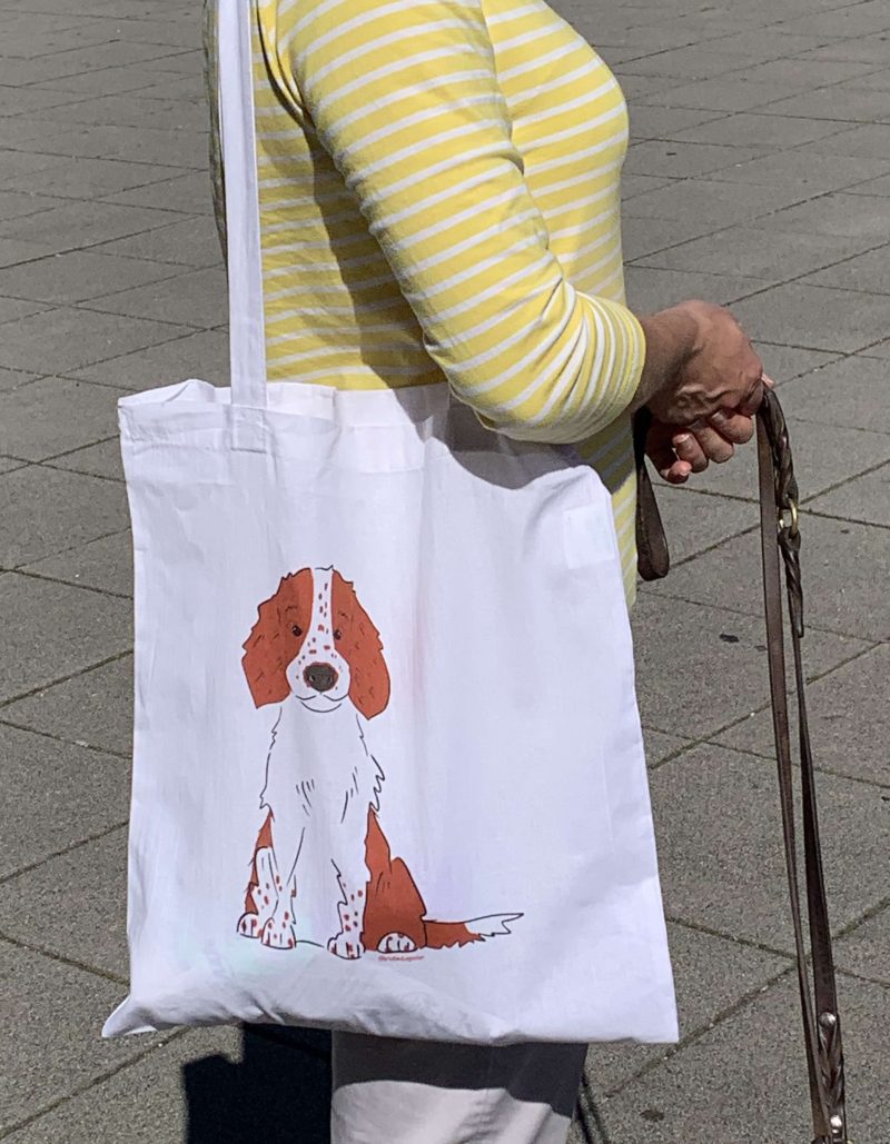 Frau trägt bedruckte, weiße Tasche mit Henkeln mit einem Welsh Springer Spaniel Welpen